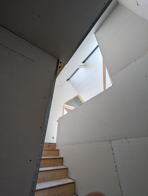 Unfinished stairs leading to a bright upper area with drywall.
