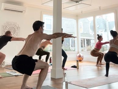 People practicing yoga poses in a bright studio with large windows.