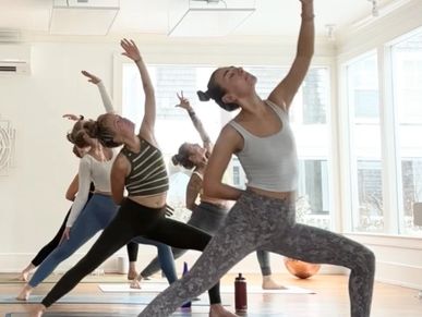 Group yoga session with participants stretching in a bright studio.