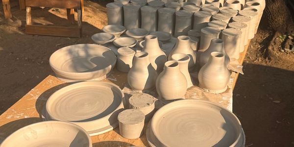 Unpainted pottery including bowls, plates, and jugs drying in the sun.
