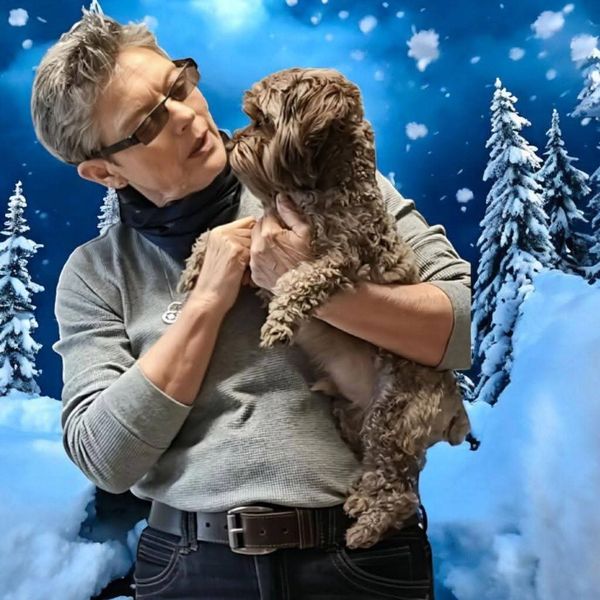 Person holding and looking affectionately at a small dog in a snowy, winter background.