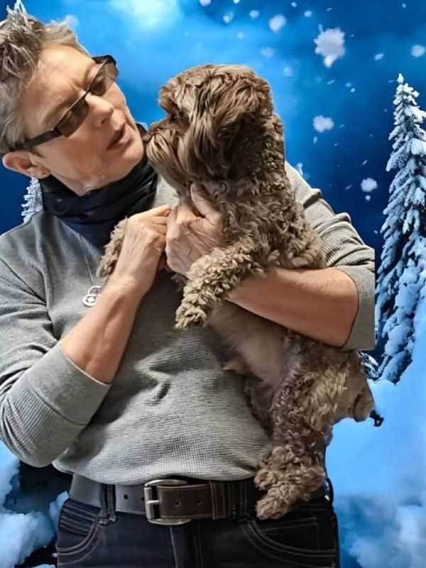 Person holding and looking affectionately at a small brown dog in a snowy winter scene.