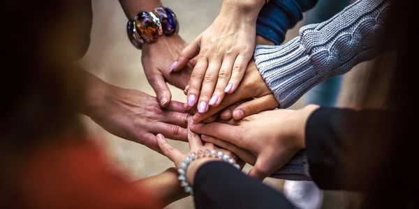 Multiple hands stacked together symbolizing unity, teamwork, and personal care.