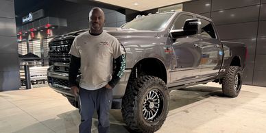Man standing next to a lifted black pickup truck at night.