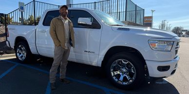 Man standing next to a white Ram pickup truck in a parking lot under clear sky.