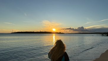 Person watching a sunset over calm ocean waters.