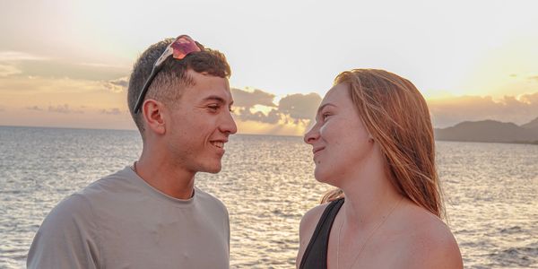 A couple smiling at each other by the sea during sunset.