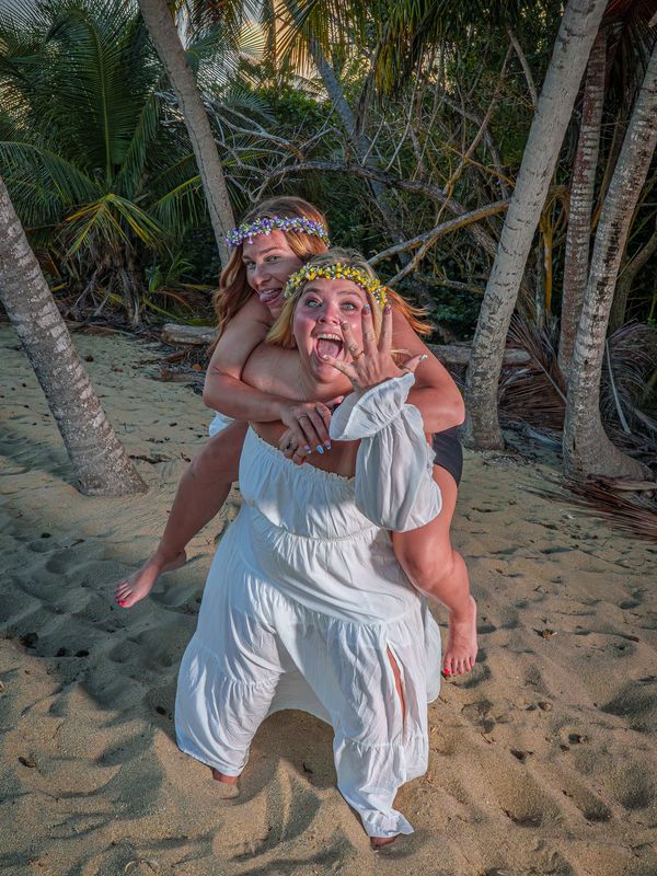 Two women having fun on a sandy beach with flower crowns.