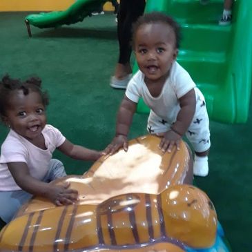 Two toddlers playing joyfully on a playground slide structure.