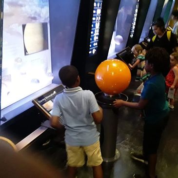 Children exploring a space exhibit with interactive displays and a glowing orange sphere.