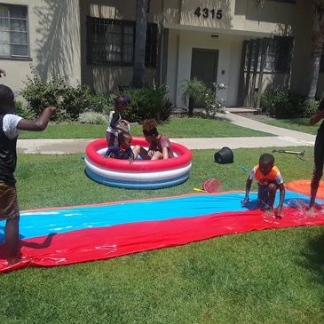 Children playing outdoors with a slip-and-slide and a small inflatable pool.