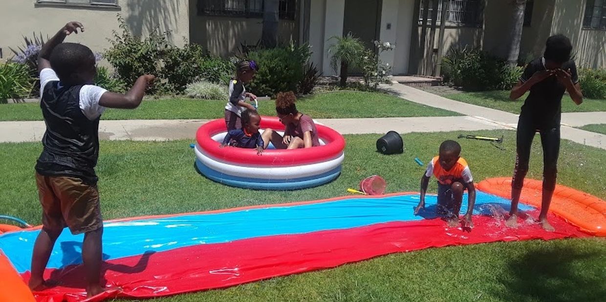 Children playing on a slip and slide and in a small pool outdoors.