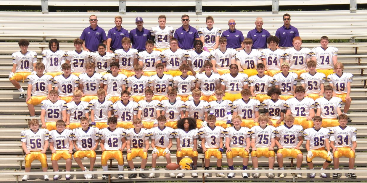 High school football team in white and yellow uniforms posing for a group photo on bleachers.
