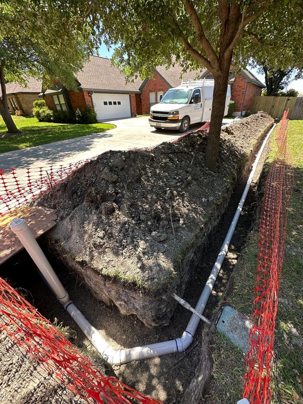 Trench with newly installed pipes beside a residential driveway.