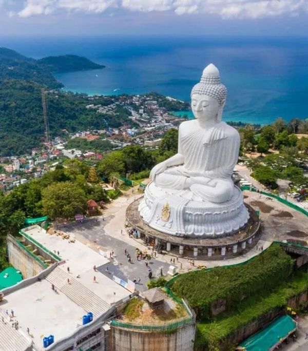 Large white Buddha statue overlooking a coastal town and ocean.