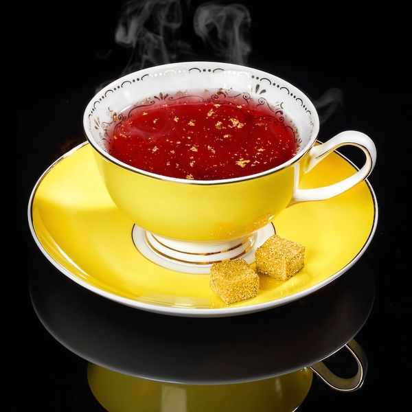 The photo shows a cup of tea with two GOLD SUGAR cubes and gold flakes.