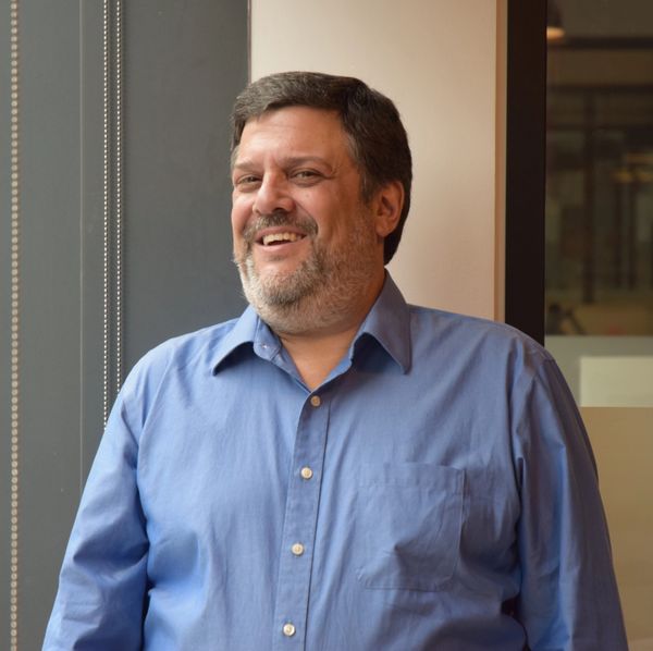 Smiling man in a blue shirt standing by a window.