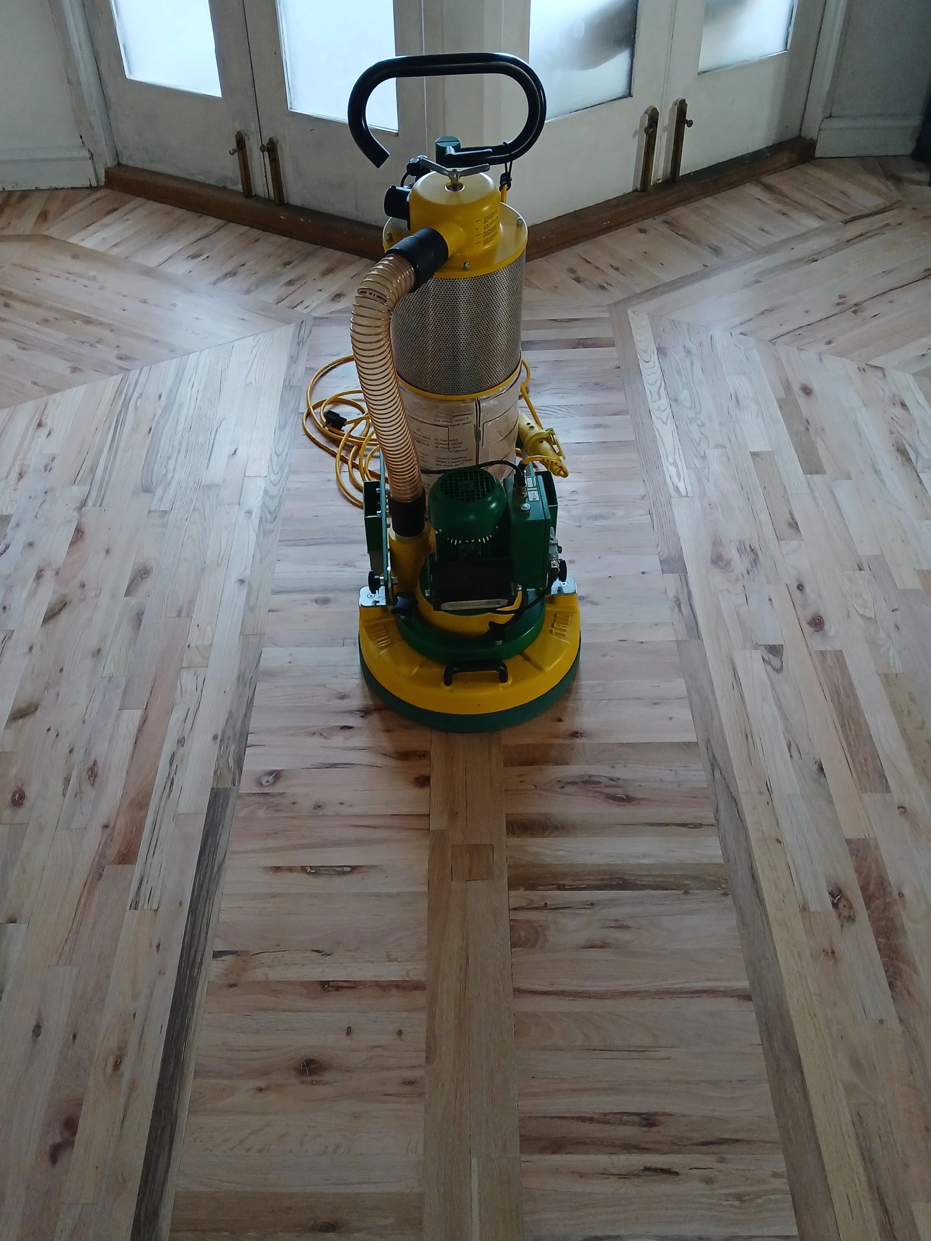 A floor sander machine on a wooden floor near glass doors.