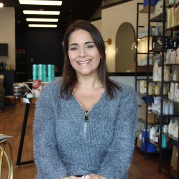 Smiling woman in a cozy gray sweater sitting in a stylish salon.