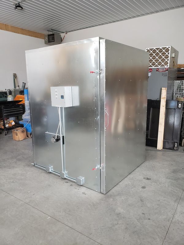 Large metallic industrial enclosure with electrical control box in a workshop.