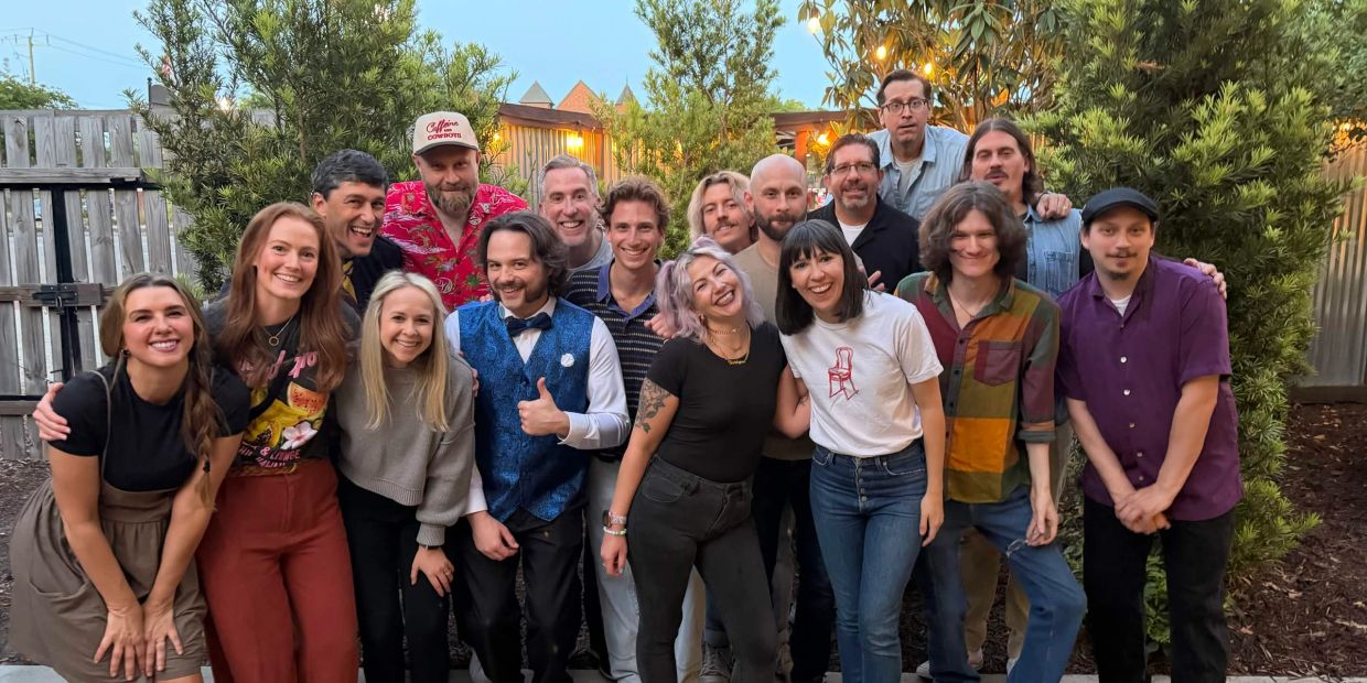 A large group of people smiling outdoors in a garden setting.