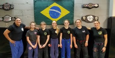 Group of martial artists posing in front of a Brazilian flag with championship belts.