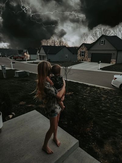Picture of a neighborhood, with two children standing outside looking at the storm rolling in. 