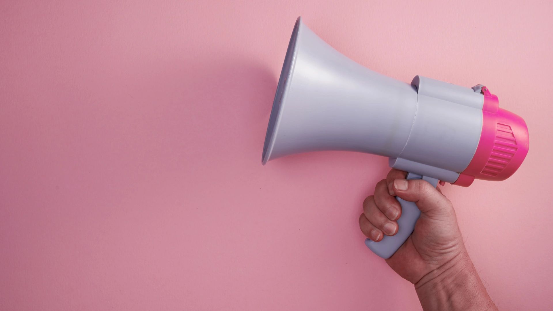 megaphone in a pink background, with a hand holding it