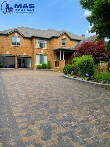 Large brick house with a patterned driveway and lush greenery.