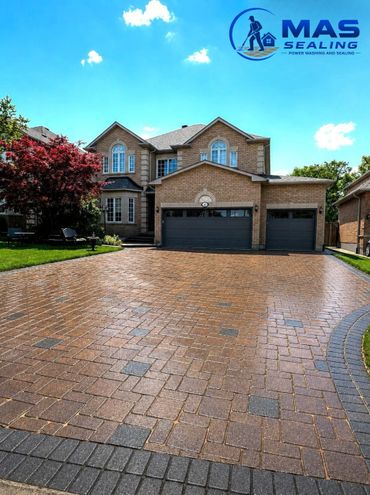 Clean, sealed driveway in front of a brick house under a blue sky.