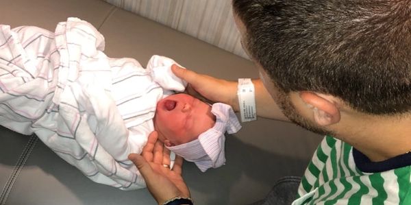 A man tenderly holds a newborn baby swaddled in a blanket.