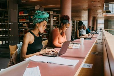 Diverse students studying with laptops in a spacious library.