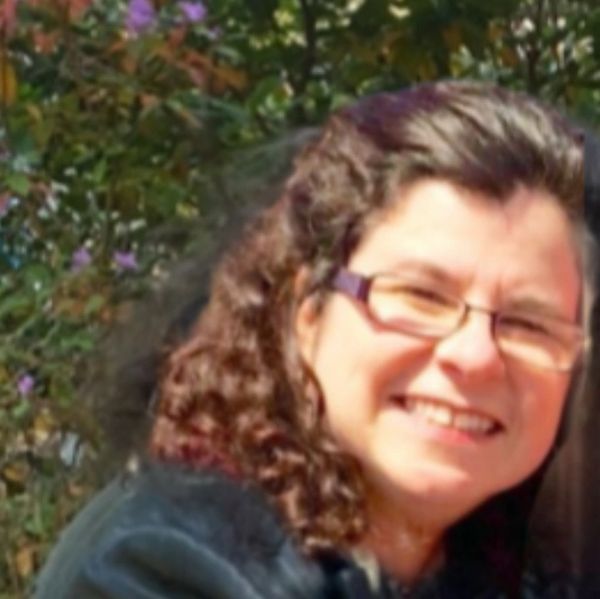 Smiling woman with curly hair and glasses outdoors.