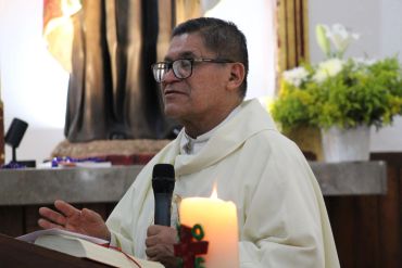 Sacerdote en ceremonia religiosa sosteniendo un micrófono.