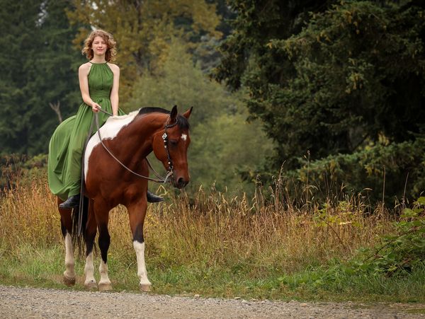 Woman in green dress riding a brown and white horse.