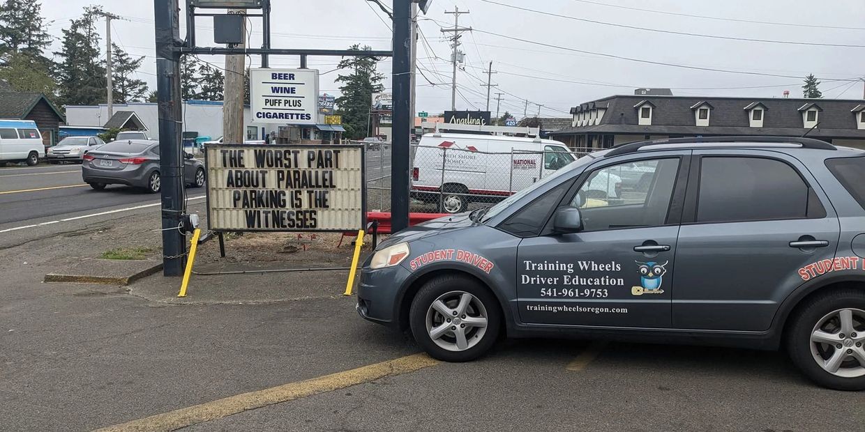 Training Wheels Driver Education car parked next to a sign that says "The worst part about parallel 