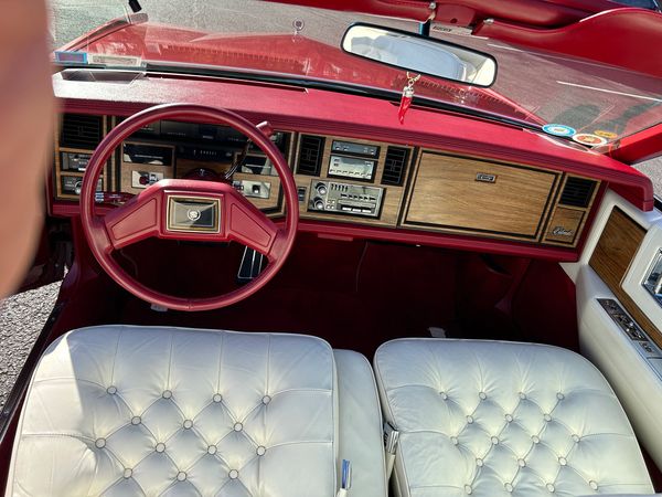 Vintage car interior with red dashboard and white tufted leather seats.