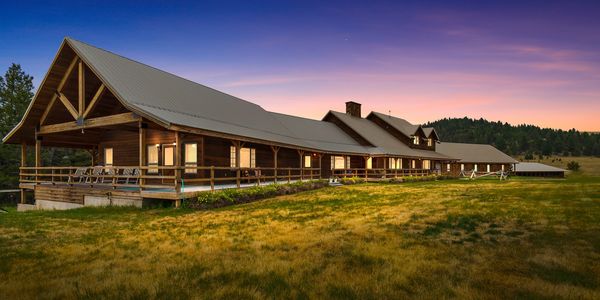 Large wooden lodge at sunset with a spacious porch and surrounding fields.