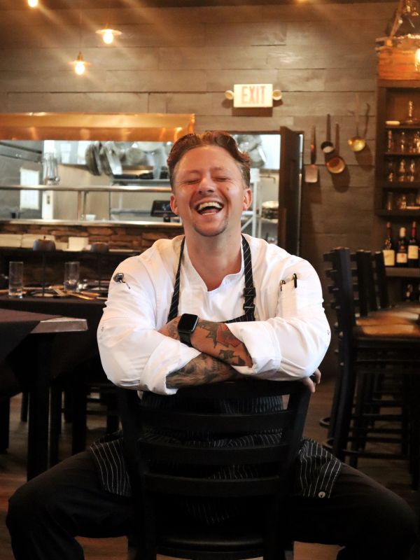 Happy chef sitting backward on a chair in a cozy restaurant.