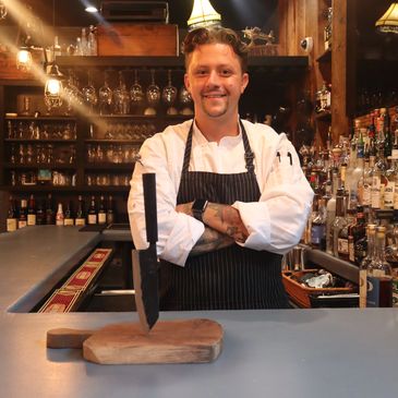 Chef posing behind a knife stuck in a cutting board.