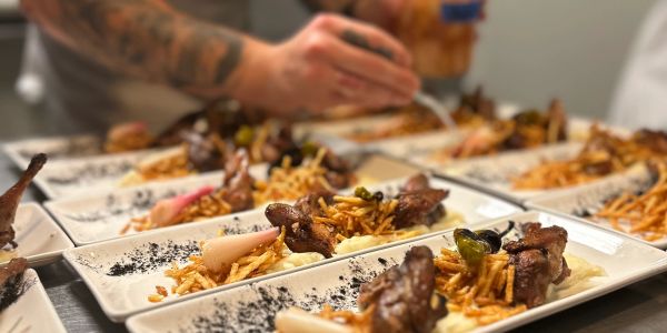 Chef plating multiple gourmet dishes with meat and fries.