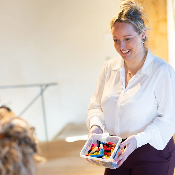 Vrouw toont een doos LEGO-steentjes met een glimlach.