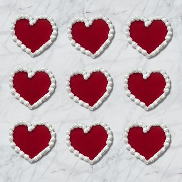 Nine red heart shapes outlined with white cream on a marble surface.