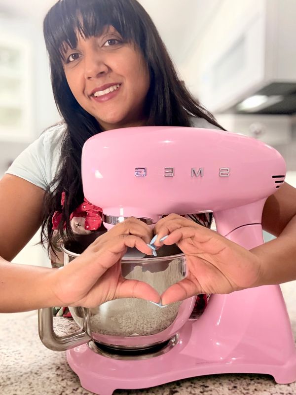 Woman smiling with a pink SMEG mixer, making a heart with her hands.