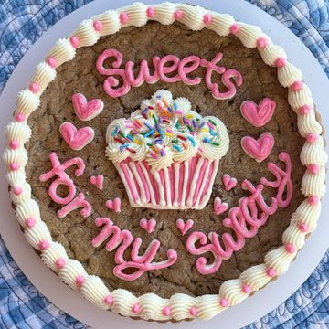 Large cookie cake decorated with pink frosting and a cupcake design.