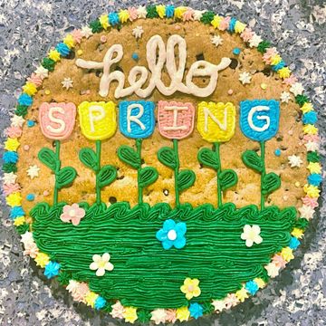Decorated cookie saying 'hello SPRING' with colorful flowers and green grass.