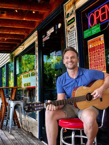 JD Mahan sitting outside Dee’s Country Cocktail Lounge in Madison, Tennessee with an acoustic guitar.