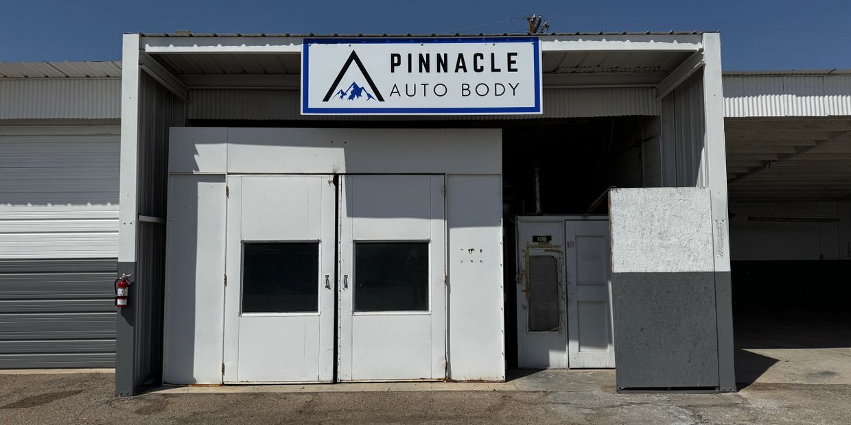 Exterior of Pinnacle Auto Body shop with white double doors and clear signage.