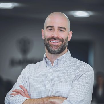 Smiling bald man with beard crossing arms.