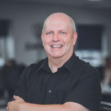 Smiling bald man in black shirt with arms crossed.